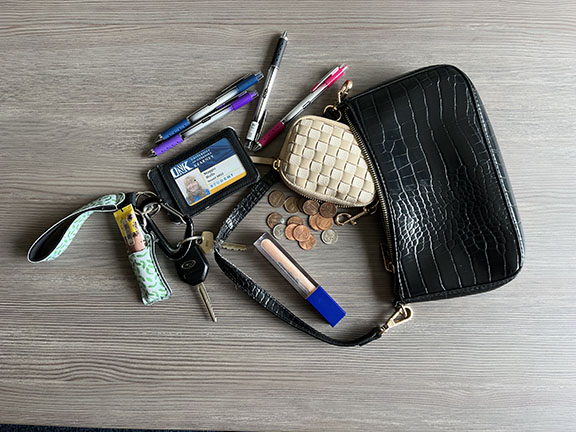 Black purse with contents like keys, lip gloss, coins, and pens spilling out